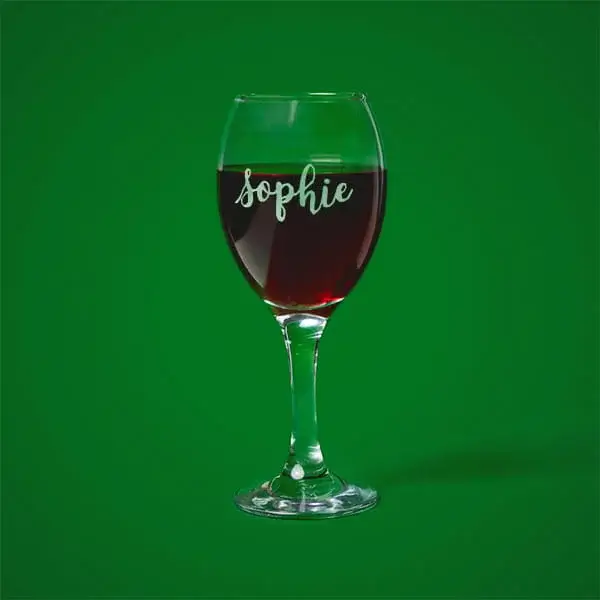 Personalised engraved wine glass featuring a custom name, displayed against a green background.